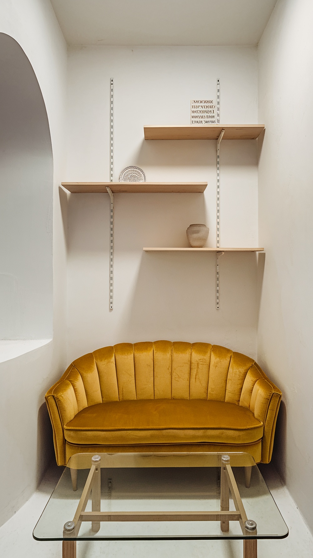 A yellow velvet sofa in a small living room with simple shelves.